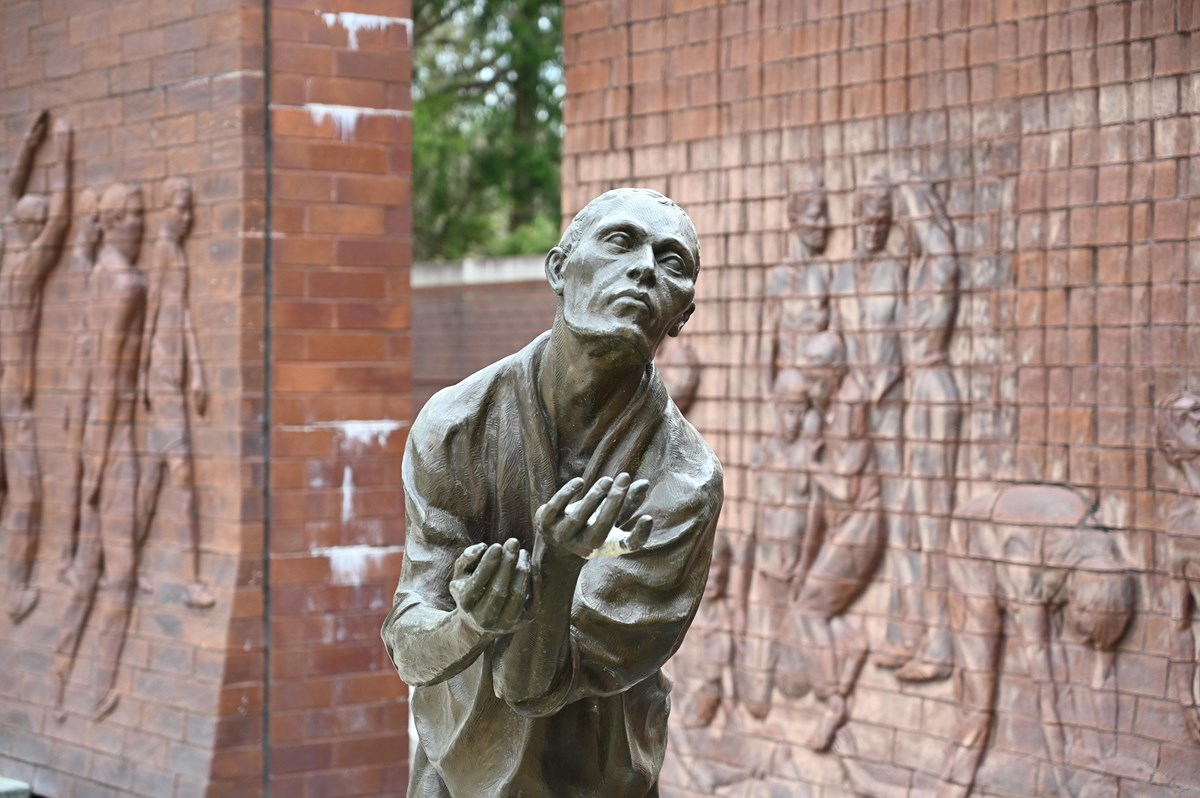 stone statue stands with his arms stretched forward. Two large stone walls sit behind him.