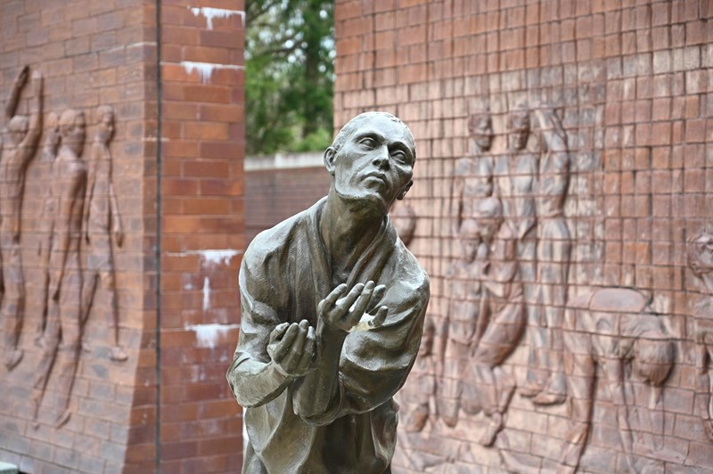 stone statue stands with his arms stretched forward. Two large stone walls sit behind him.