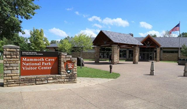 A brown park entrance sign with a large building in the background