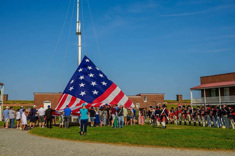 Flag Change Program Visitors hold the edges of a large American flag as it is raised on to a large flagpole