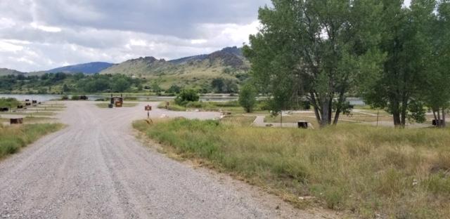 Looking down the gravel drive with campground sites on both sides and pit toilet.