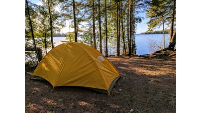 Yellow Tent in a campsite along Lake Superior with trees along the shoreline.