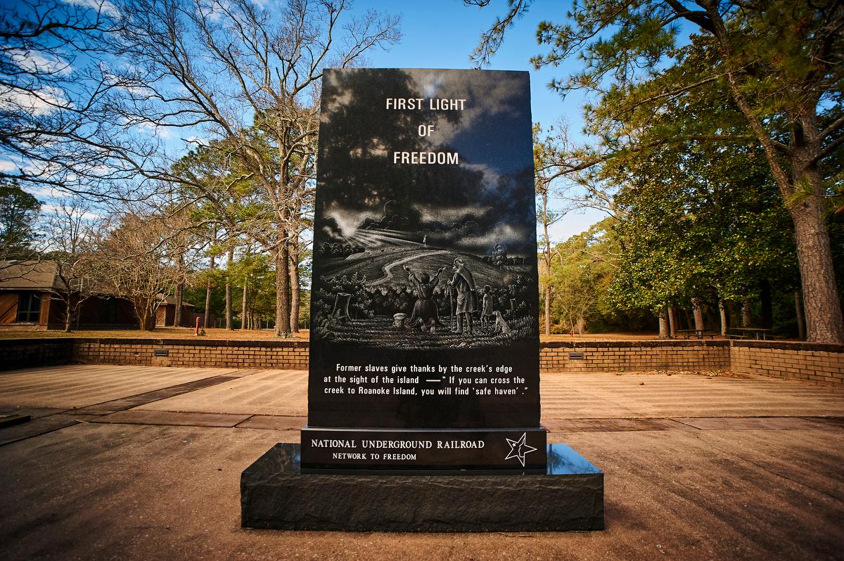 A black stone monument with the words "First Light of Freedom and an etched painting of many people