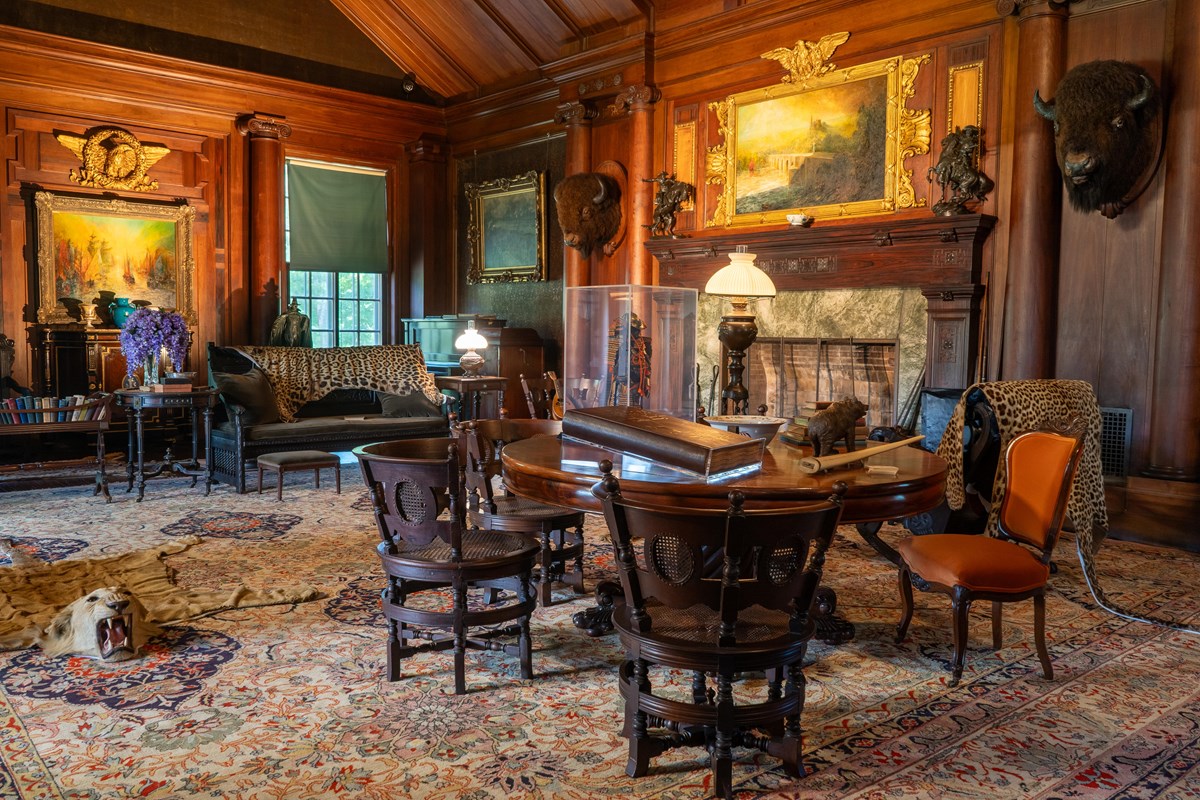 A room with mementos and animal trophies with a table and chairs in the foreground.