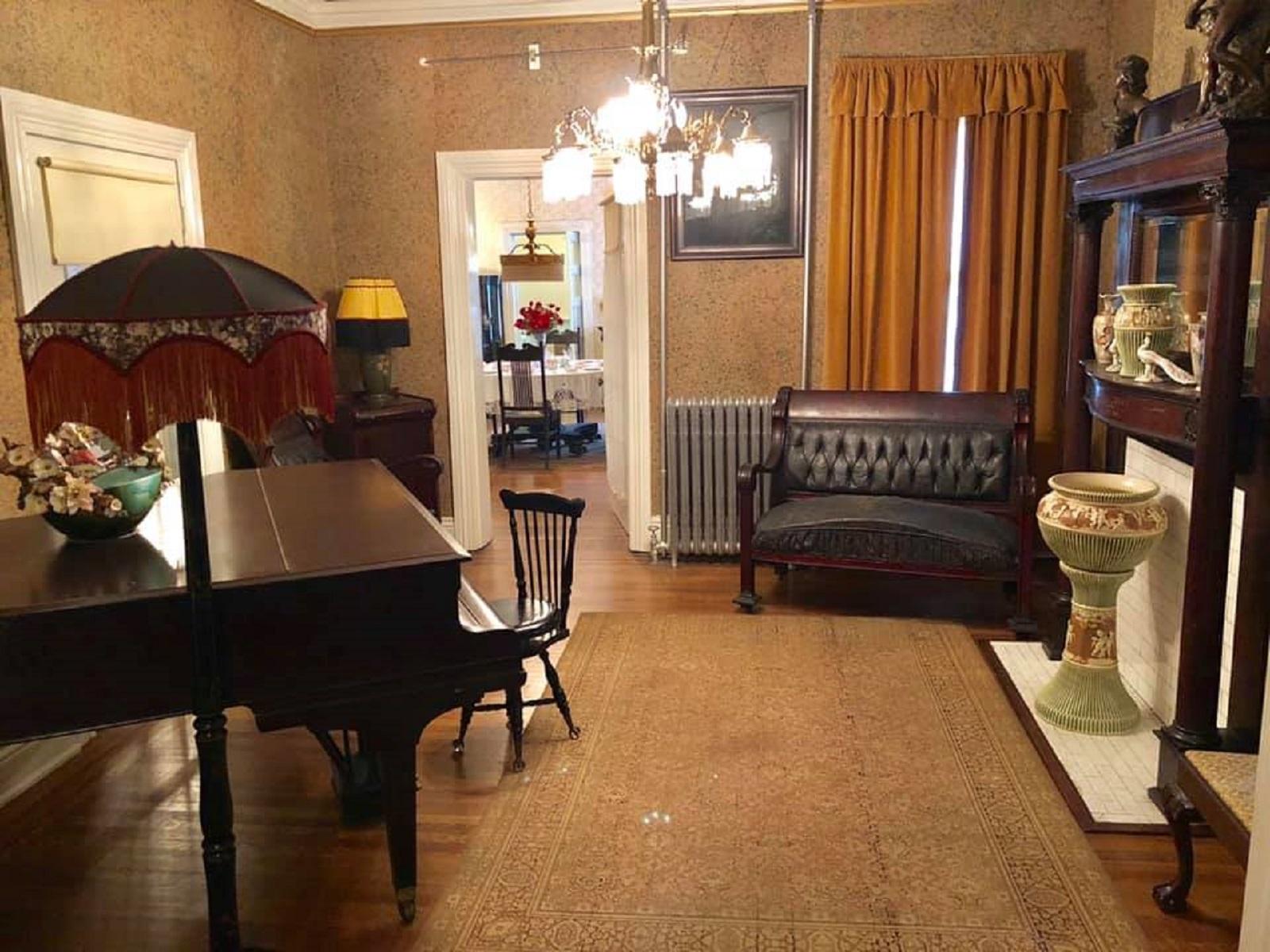 The back parlor with piano, couch, floor lamp and fireplace