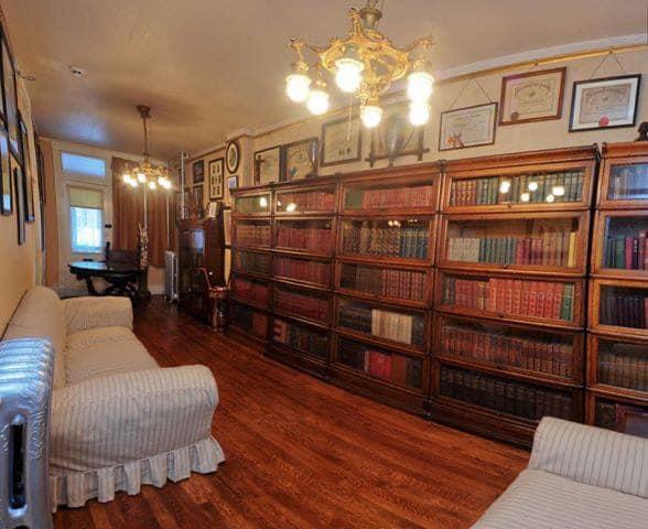 A room with a wall of full bookcases, chairs and several diplomas on the wall