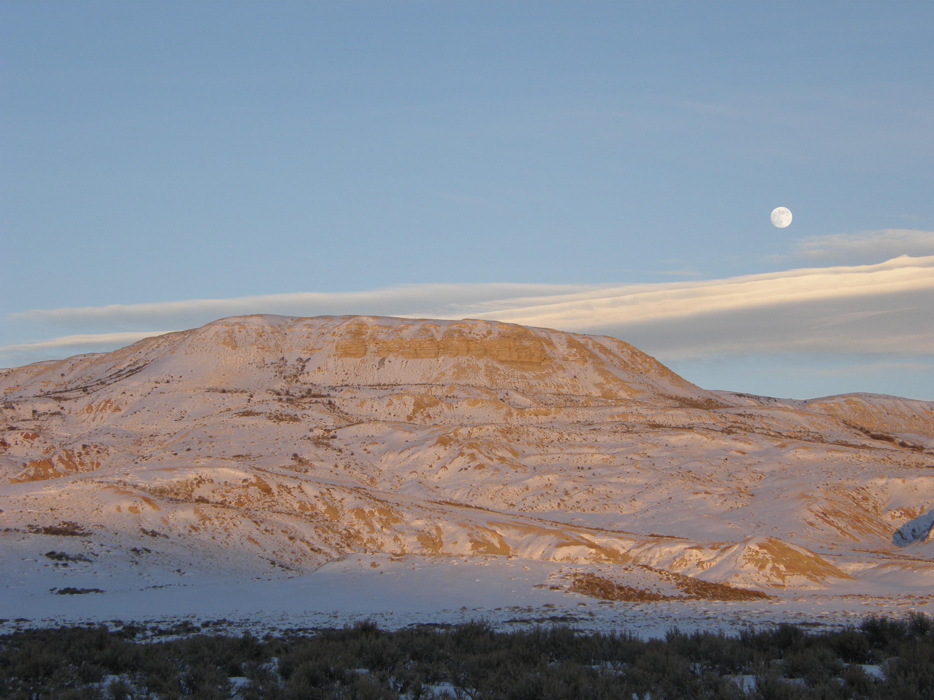 The moon rises just to the right of snow-covered Fossil Butte.