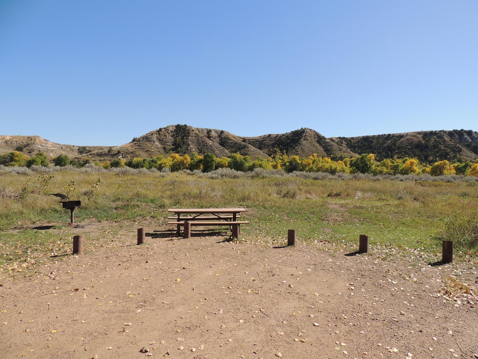A campsite in an open, grassy area with buttes and fall leaves in the background.