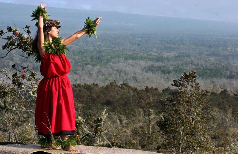 Hula at Kīlauea A hula dancer in a red dress above a forested area