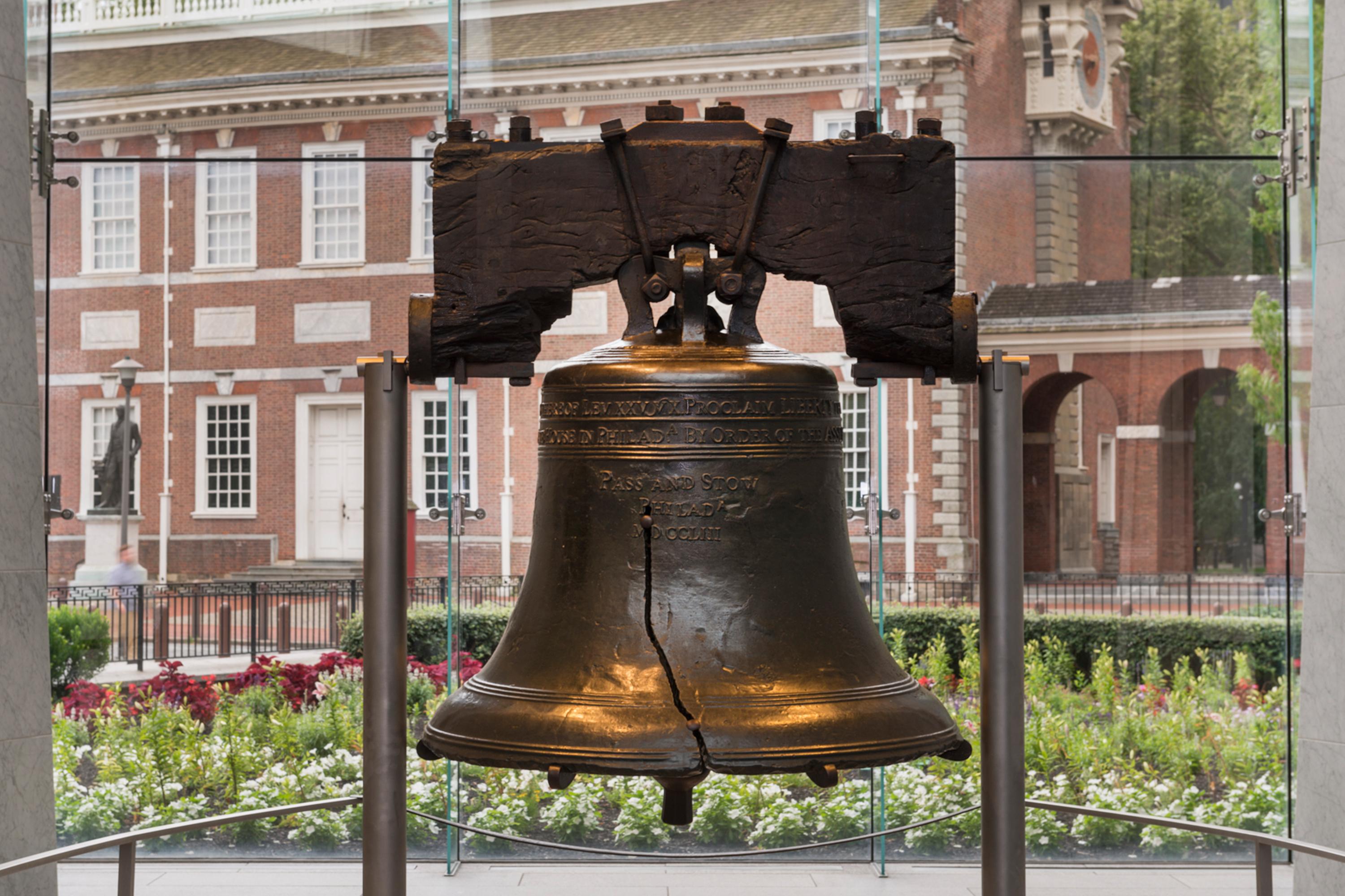Color photo of the Liberty Bell with Independence Hall in the background.