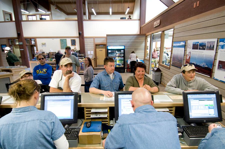 people line up at a desk in front of three uniformed people at computers