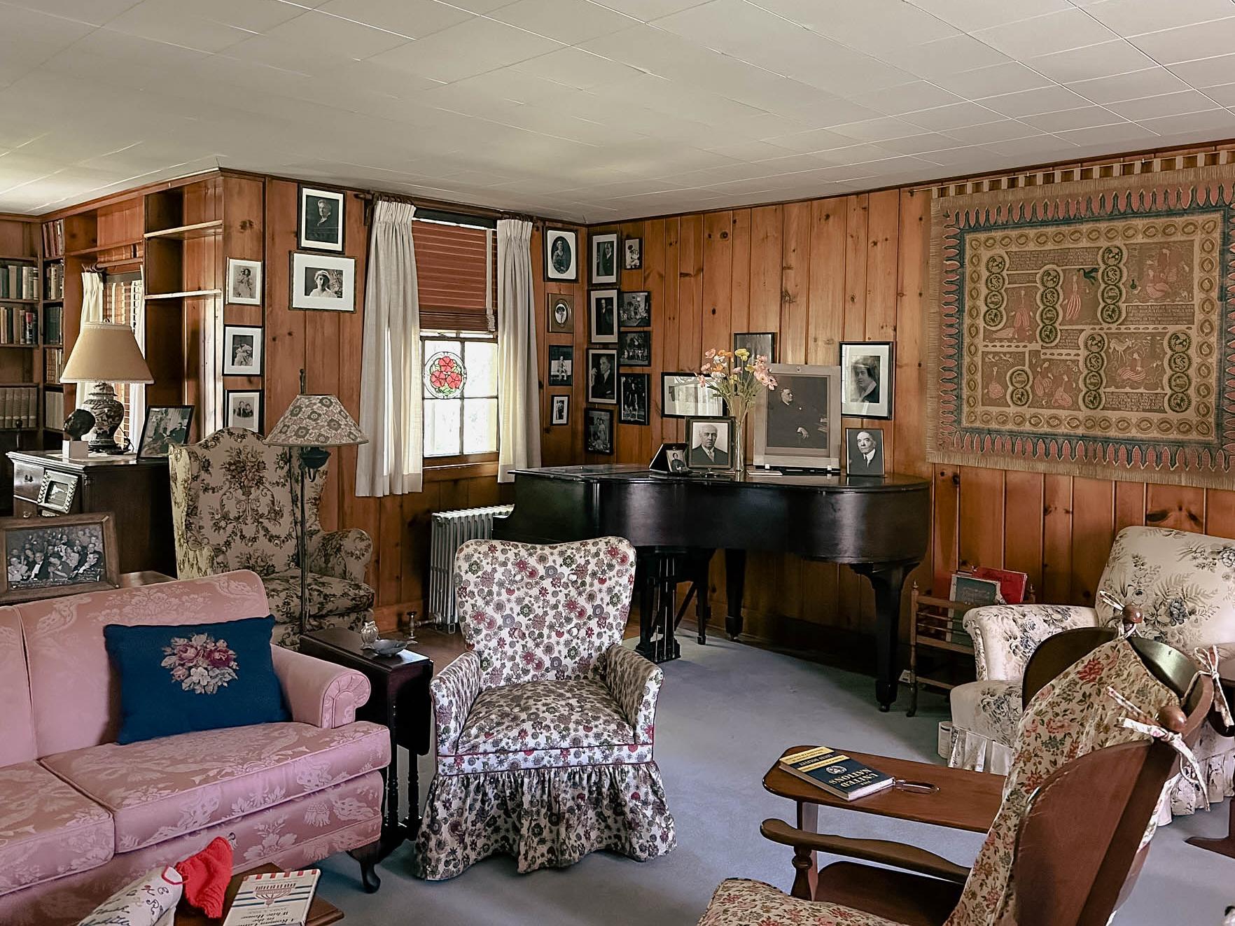 A paneled room with comfortable furniture and a baby grand piano.