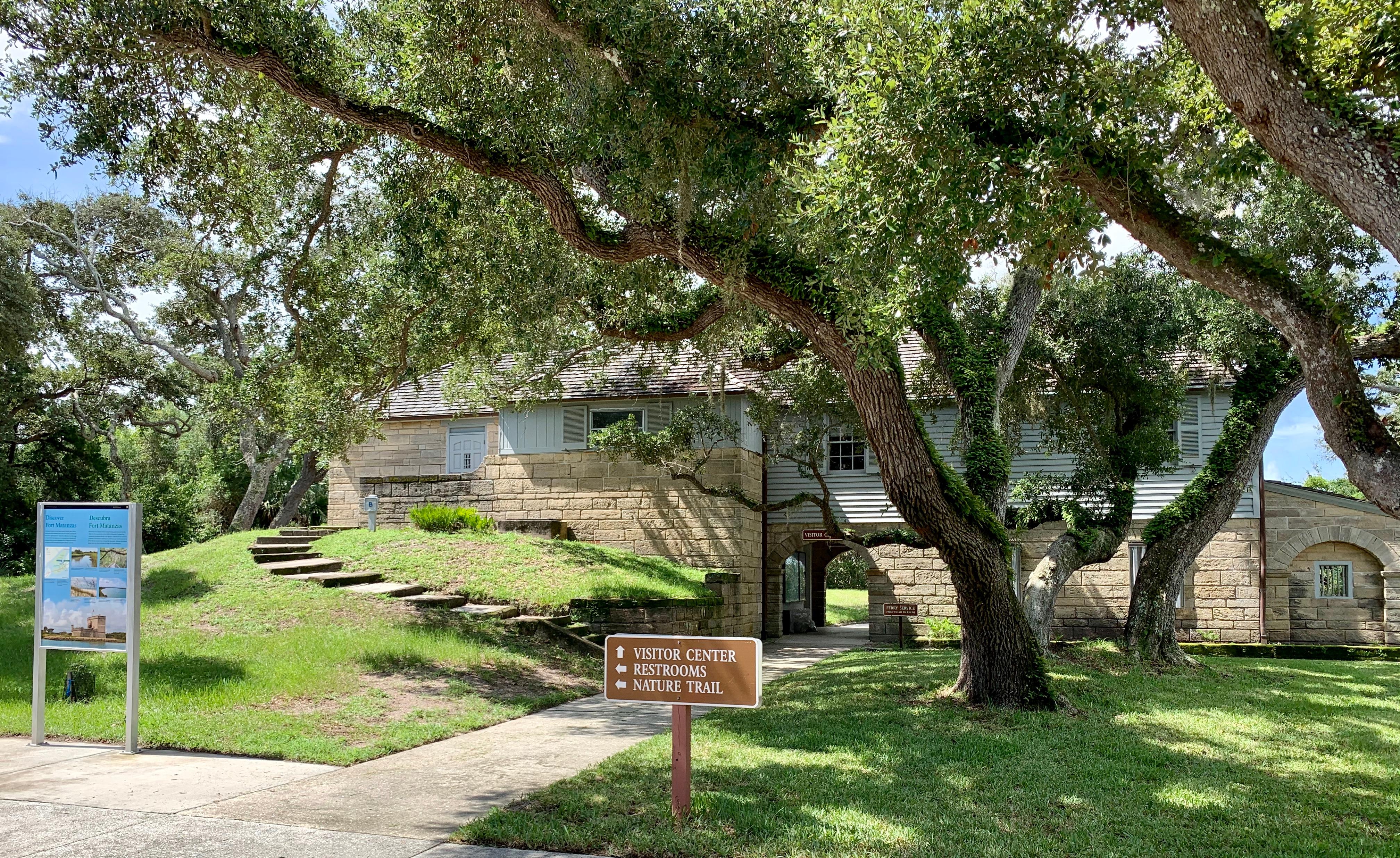 Two story building with stone base and wood second floor, oak trees, grass, two signs.