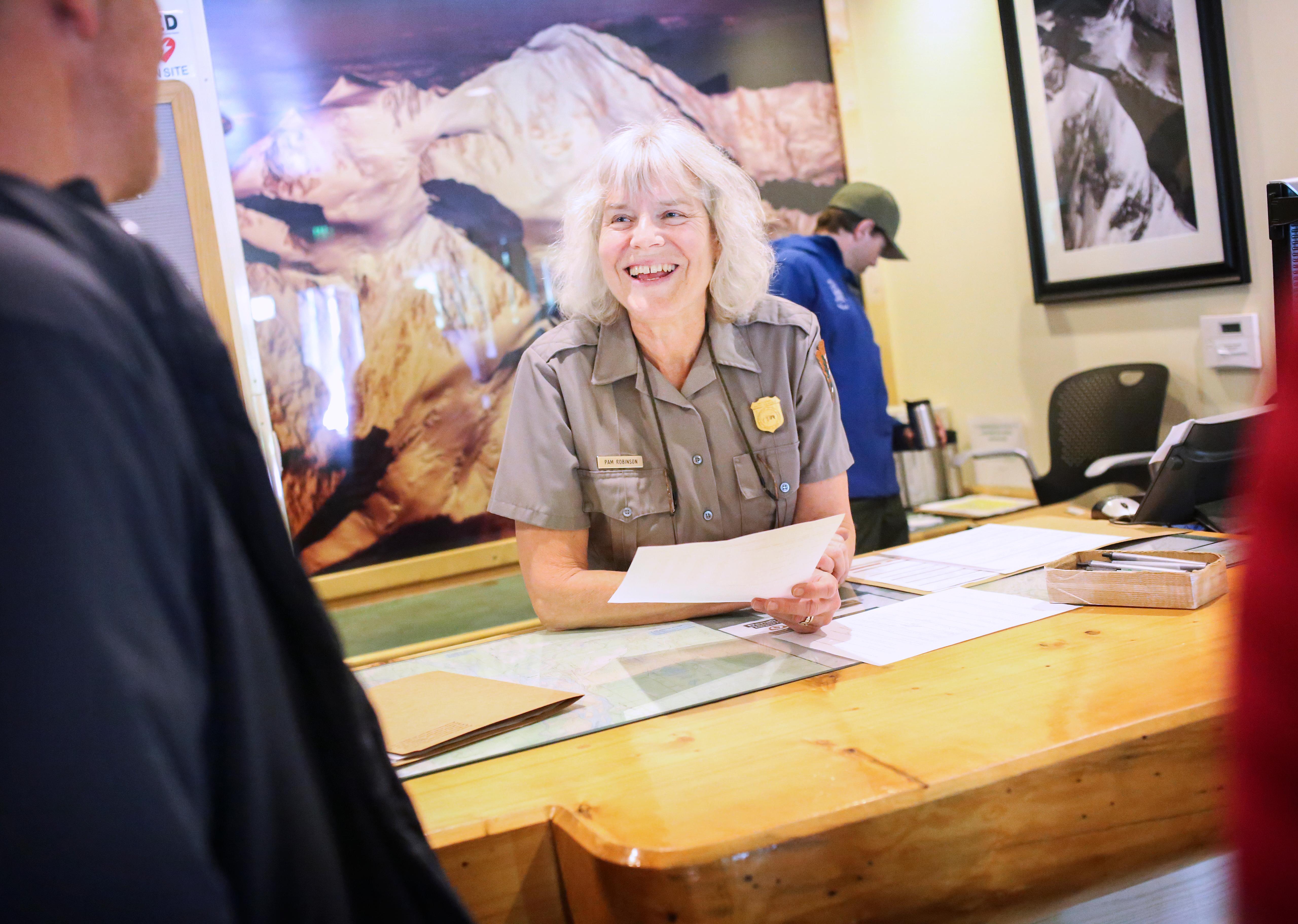 a woman in ranger uniform speaks with people at a desk indoors