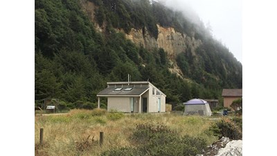 A small building and a tent are seen in front of a steep bluff.