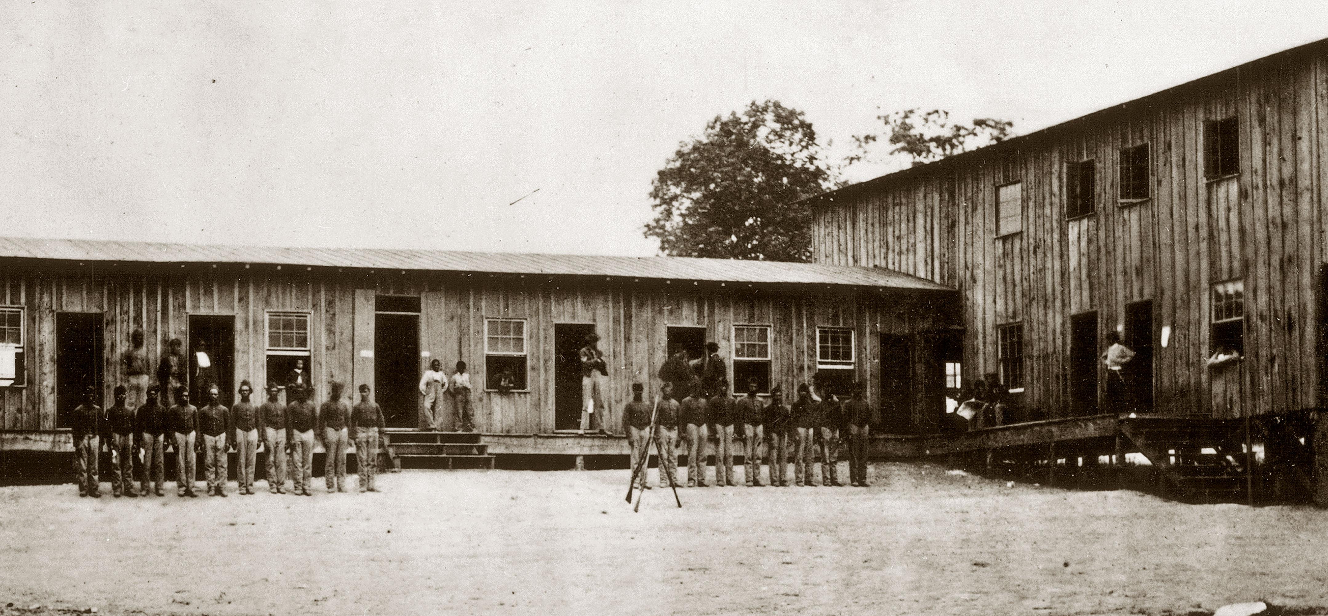 African American Civil War soldiers stand at attention outside their barracks.