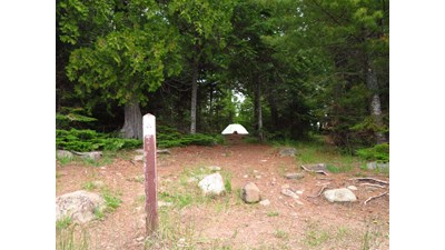 Lake Richie Canoe Campsite with sign post in foreground, tent surrounded by trees in distance.