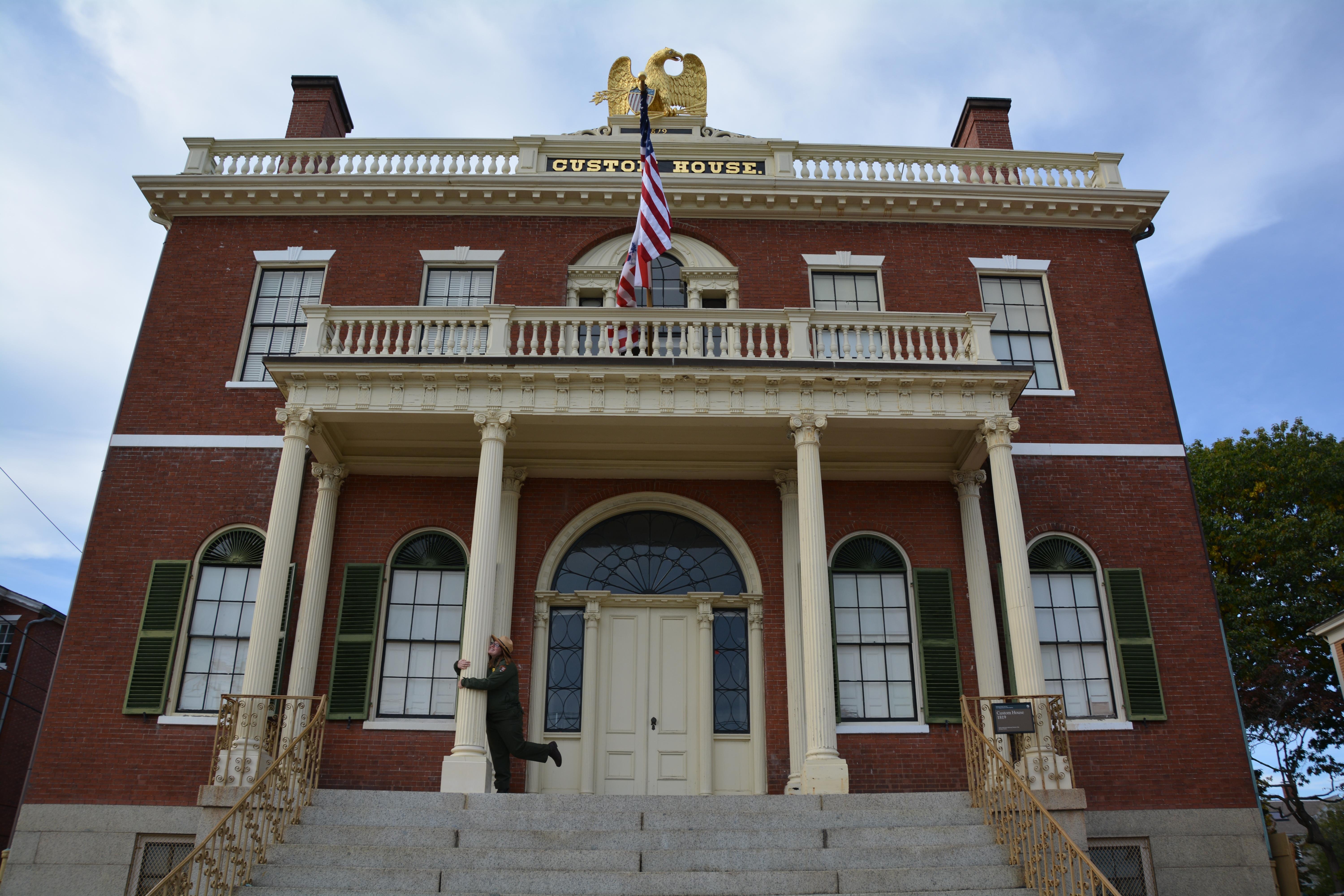Three story red brick building with white columns has a wide staircase and golden eagle on top.