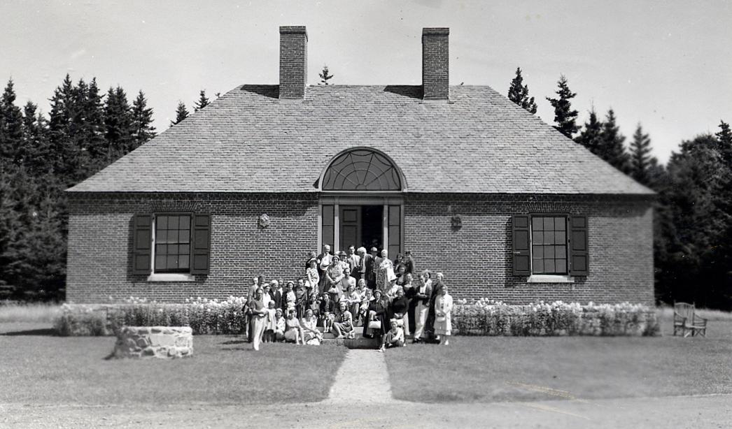 Historic brick building with slate roof, two chimneys, two windows, and a green doorway