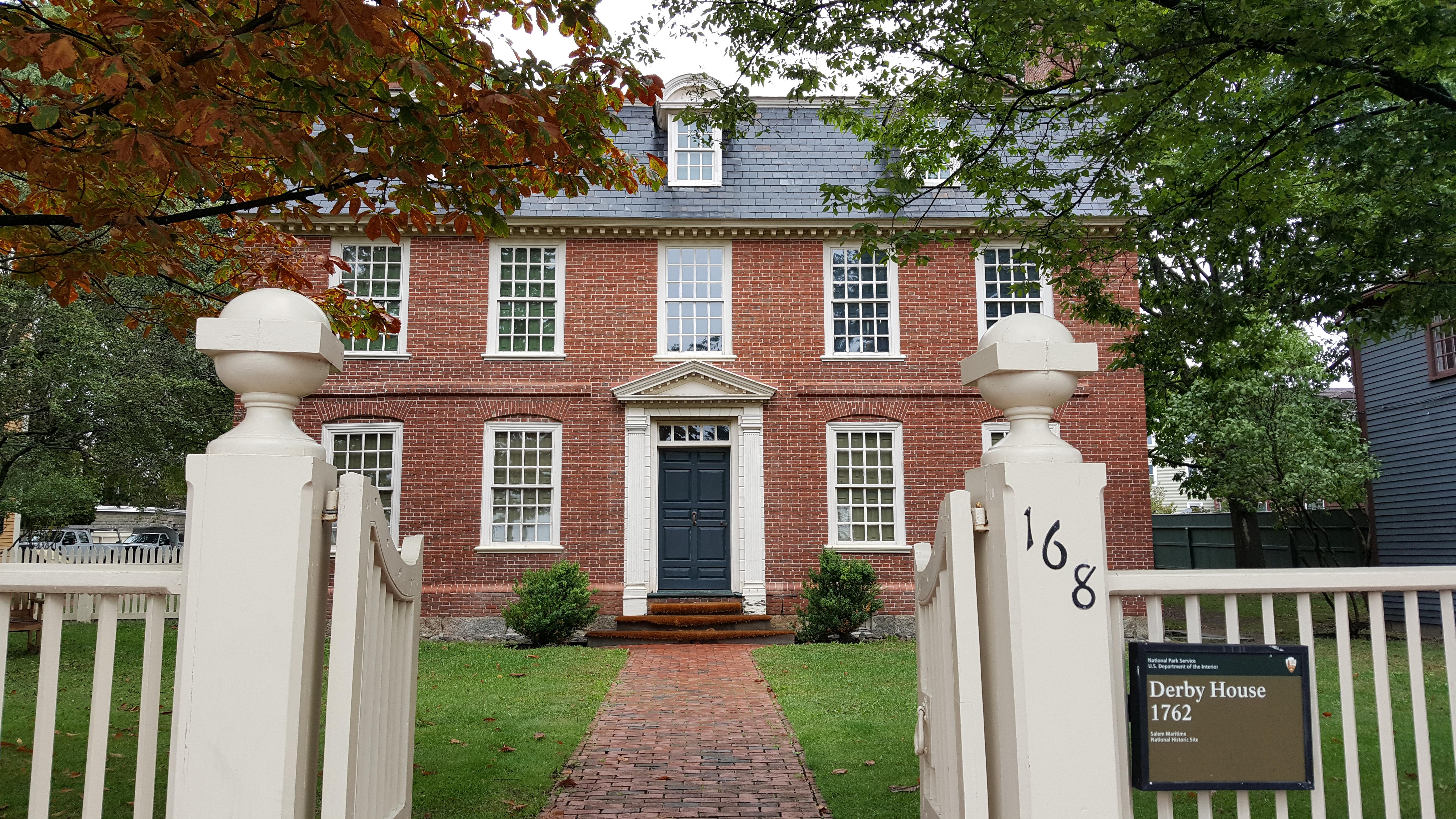 Three story red brick building with white windows and a brick pathway through grasses and trees.