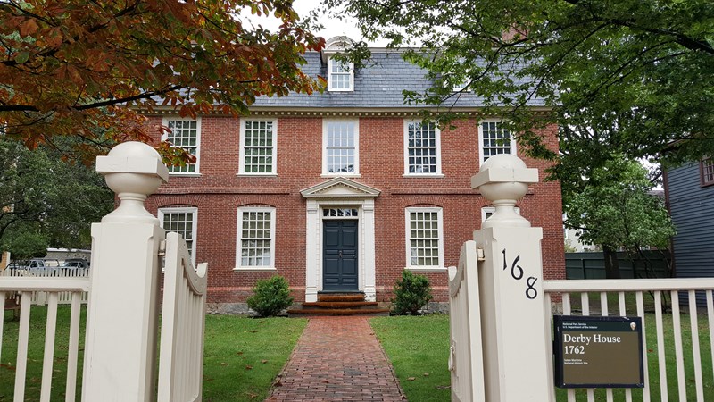 Three story red brick building with white windows and a brick pathway through grasses and trees.