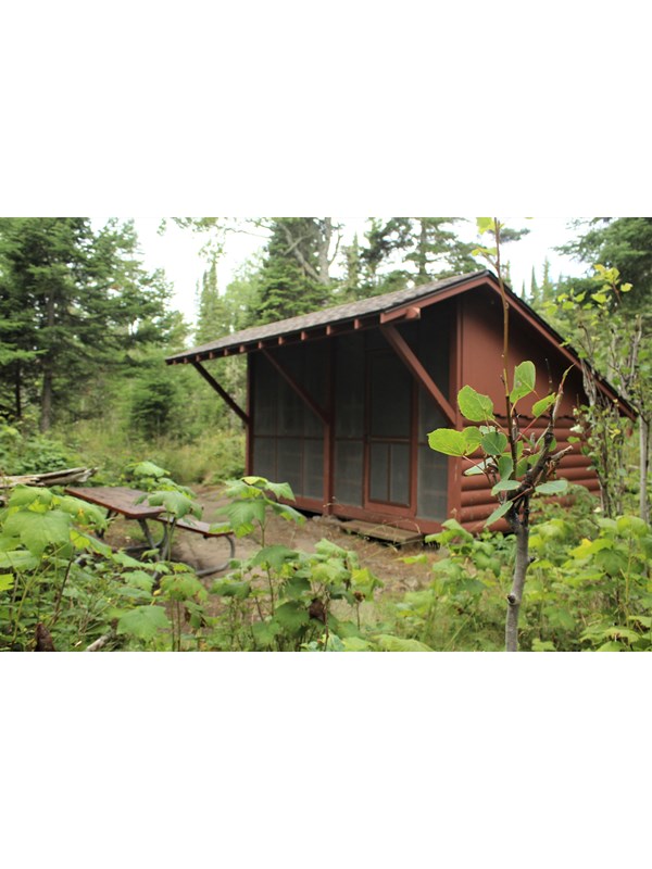 Wooden campground shelter with picnic table in front.
