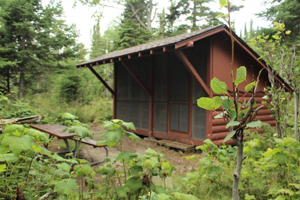 Wooden campground shelter with picnic table in front.
