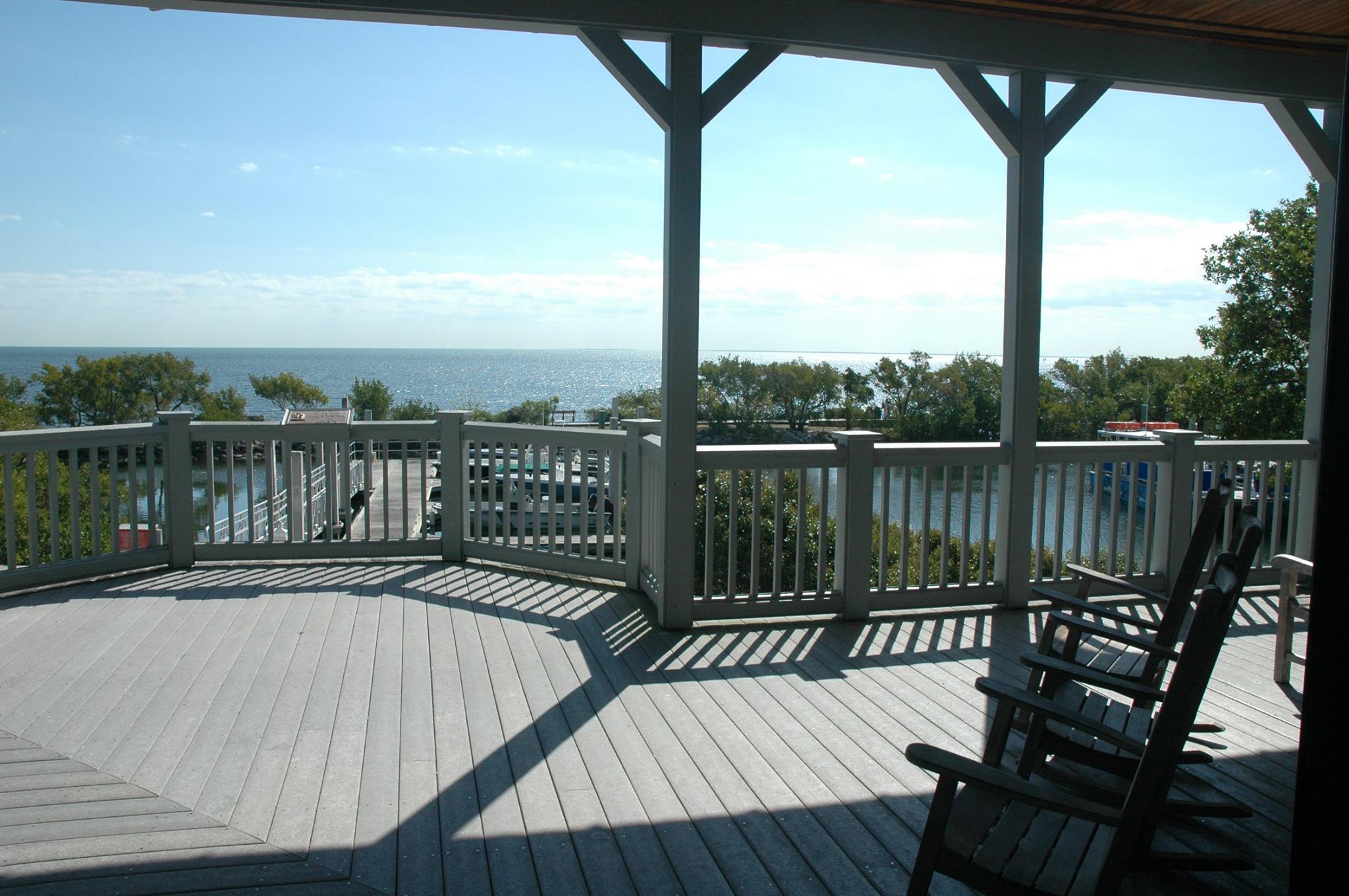 Three wooden rocking chairs on a wooden porch with a view of Biscayne Bay in the distance