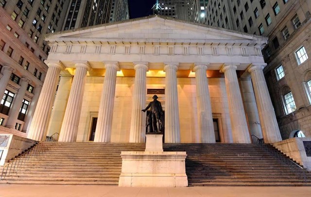 A stone, Grecian-style building, with columns and a statue in the front.
