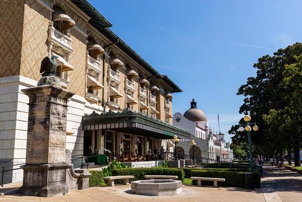 A large tan, brick building between a sidewalk and a road