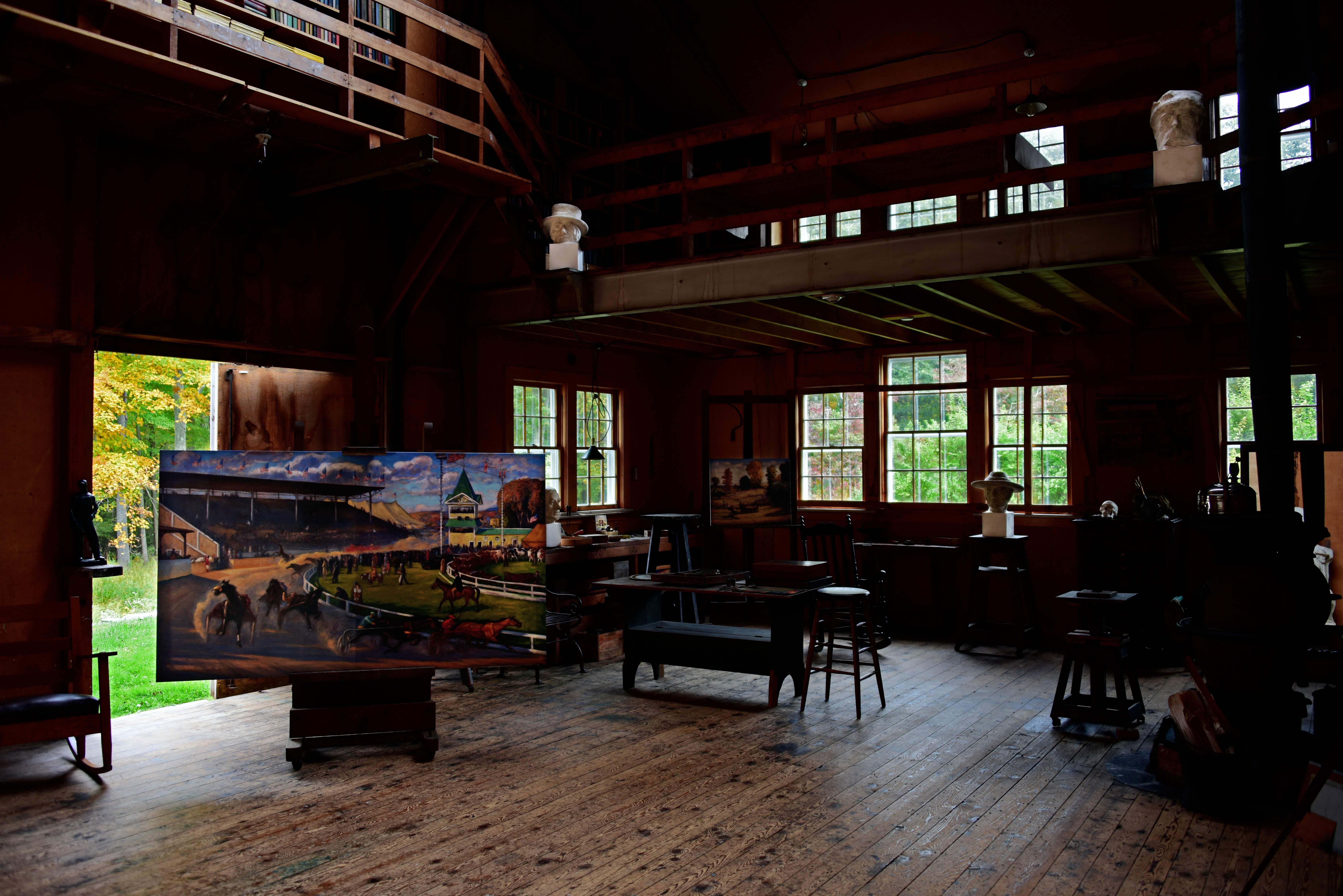 The inside of a studio with several northern windows, paintings, sculptures, and art supplies.