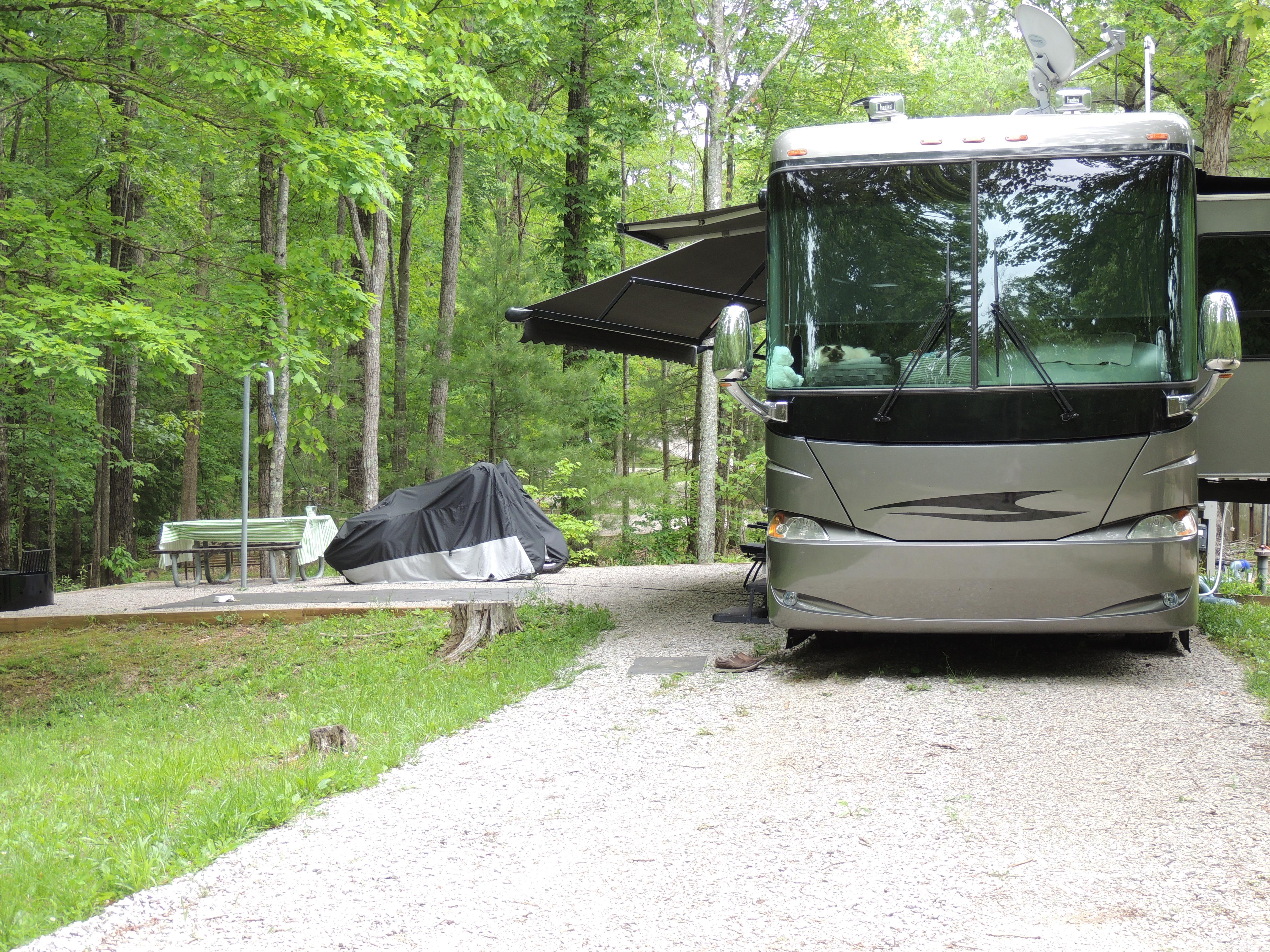 A large black RV is parked next to tent pad with picnic table.