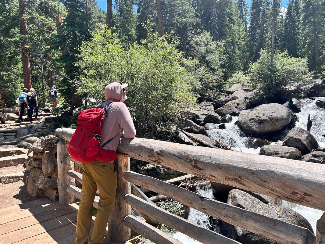 A man is standing on a bridge and looking up at a waterfall