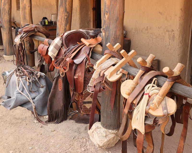 Saddles in the Plaza A row of saddles are arrayed along a wooden beam near an adobe building