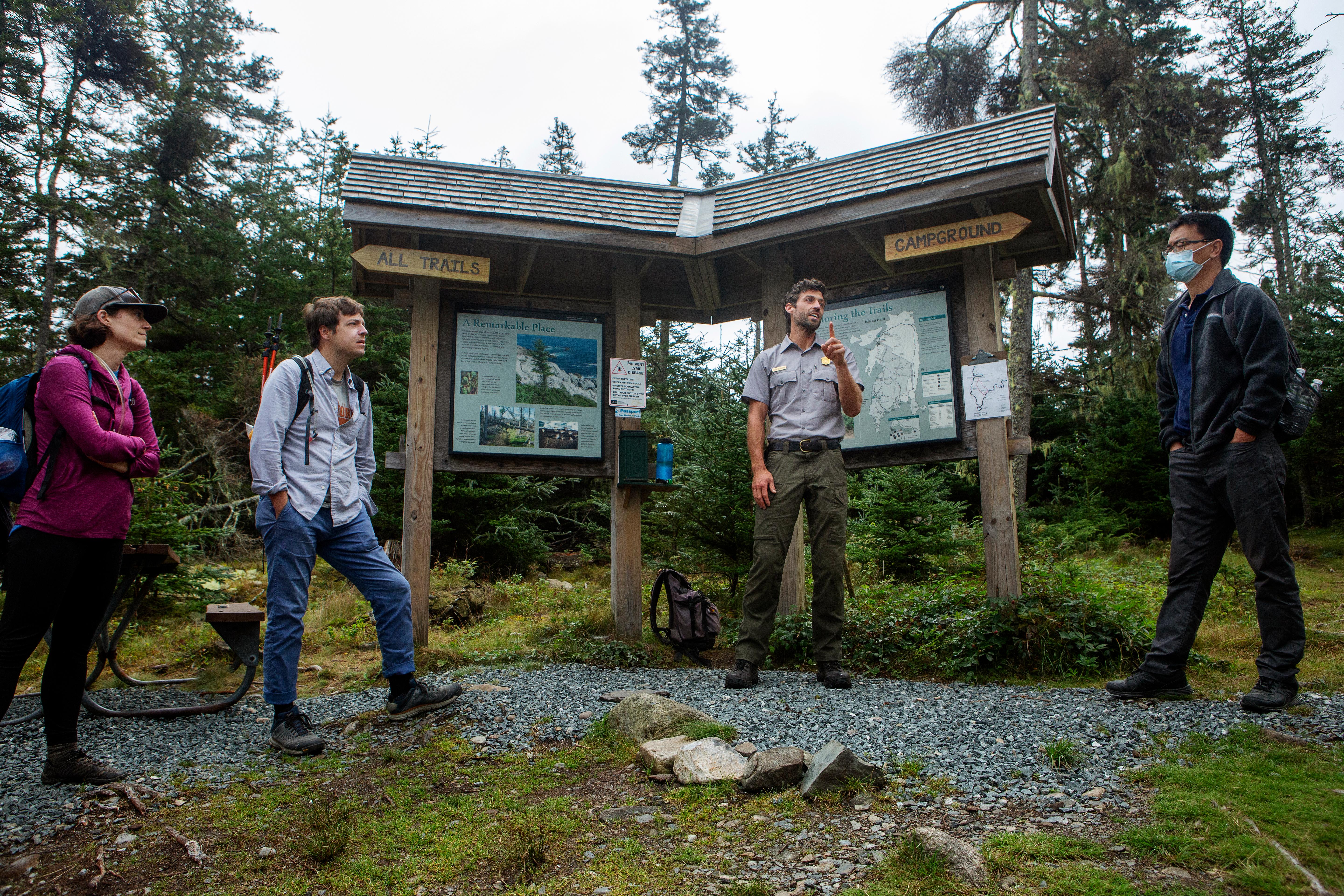 A park ranger and three other adults stand by a wood wayside with area information and directions