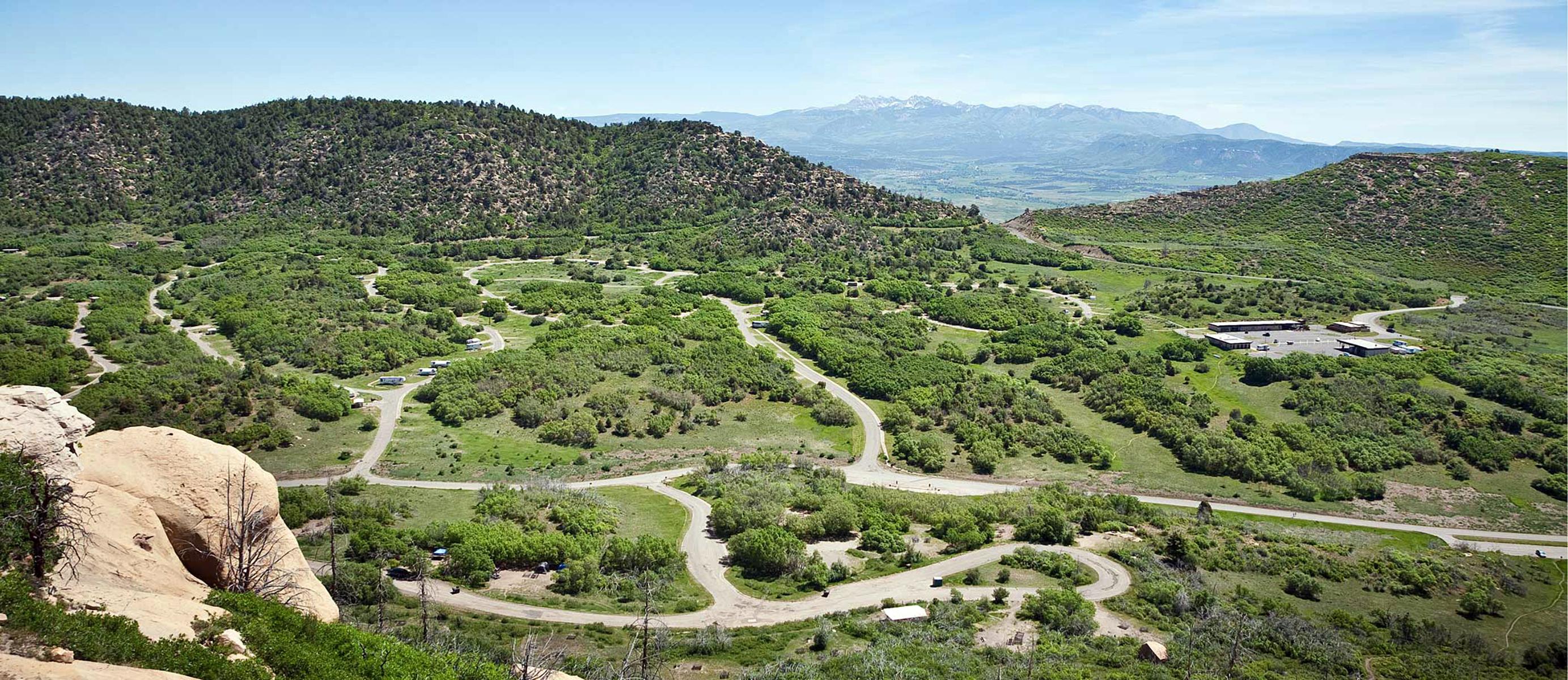Expansive, overhead view of loop roads and campsites within a green valley surrounded by hills