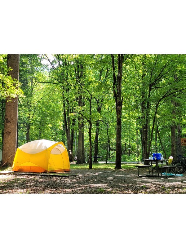 A yellow, orange, and white-colored tent on a level gravel pad near a picnic table and bikes.