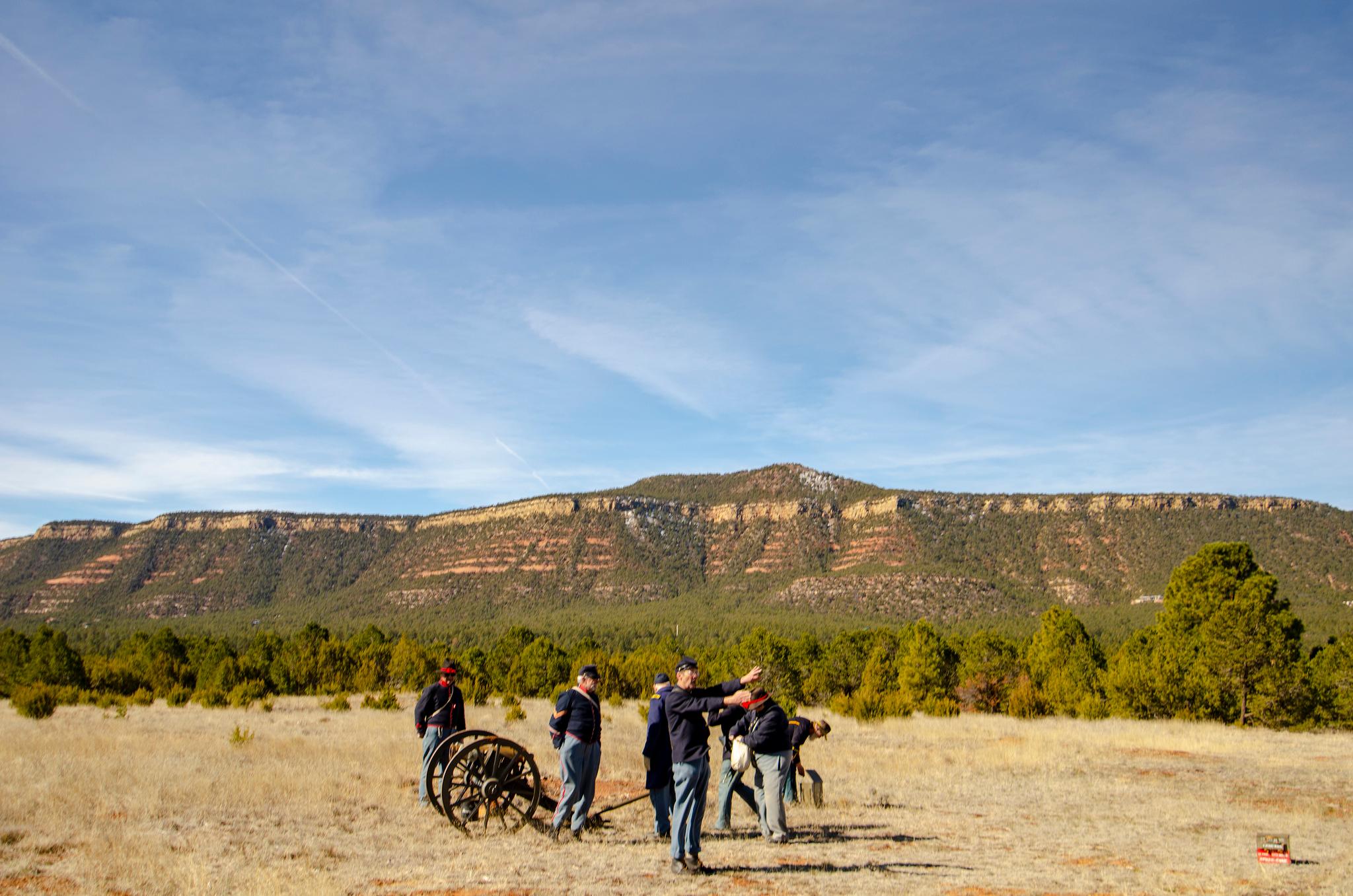 Reenactors prepare a cannon under a mesa and blue skies.