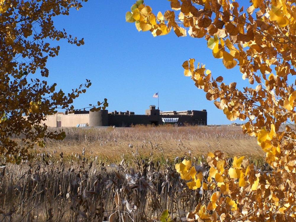 Bent's Old Fort in background with wagon in front; fall yellow cottonwood leaves in foreground
