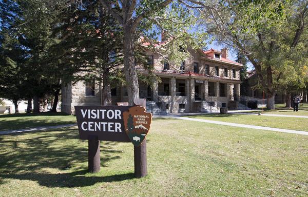 A large, brown, wooden sign stands in front of a two-story, stone building.