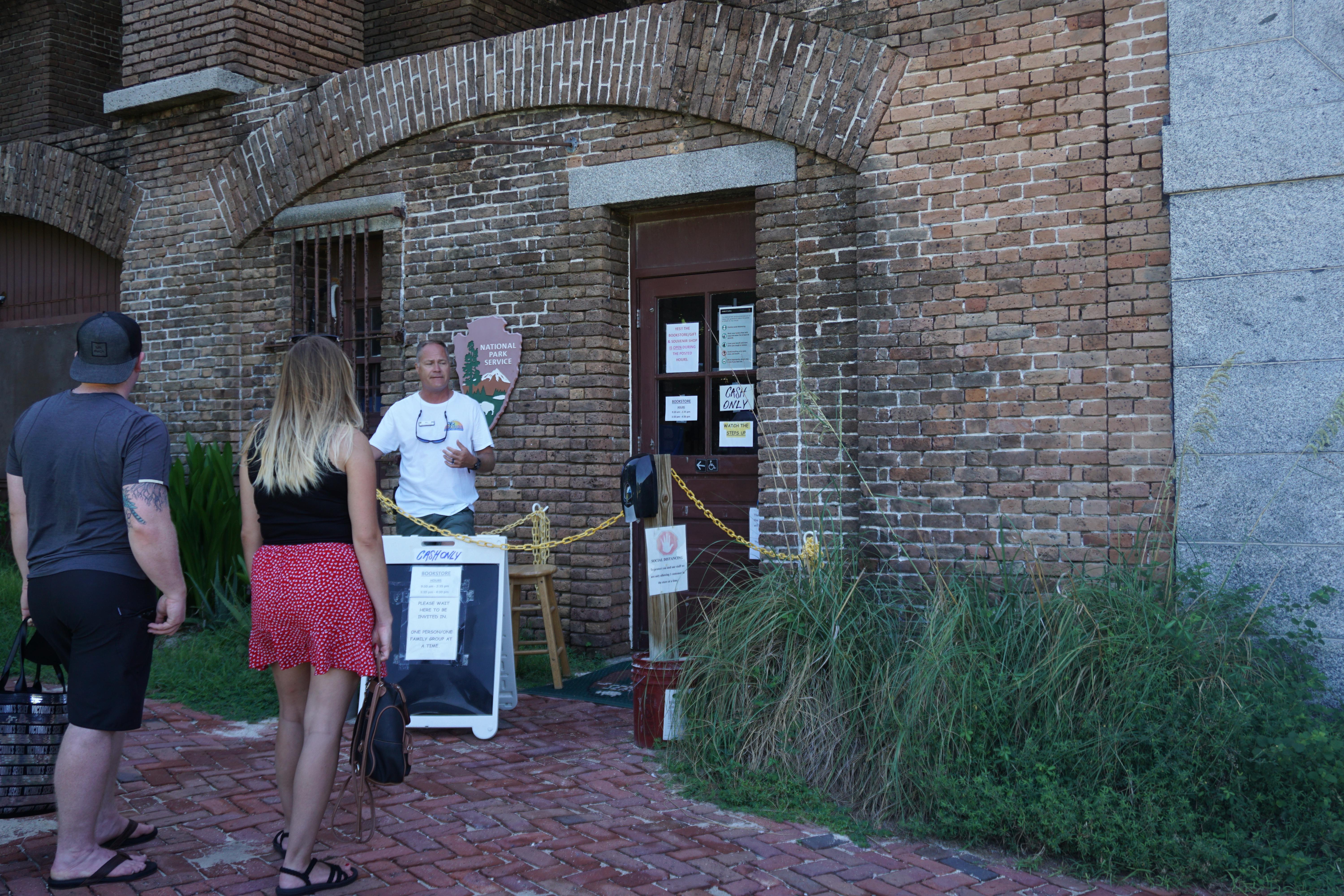 Visitors and park staff stand in front of a brown brick walled visitor center and arched doorway