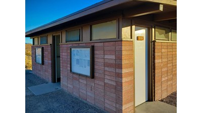 2 doors with square concrete ground pads on red brick building. 1 reads Men, other is open.