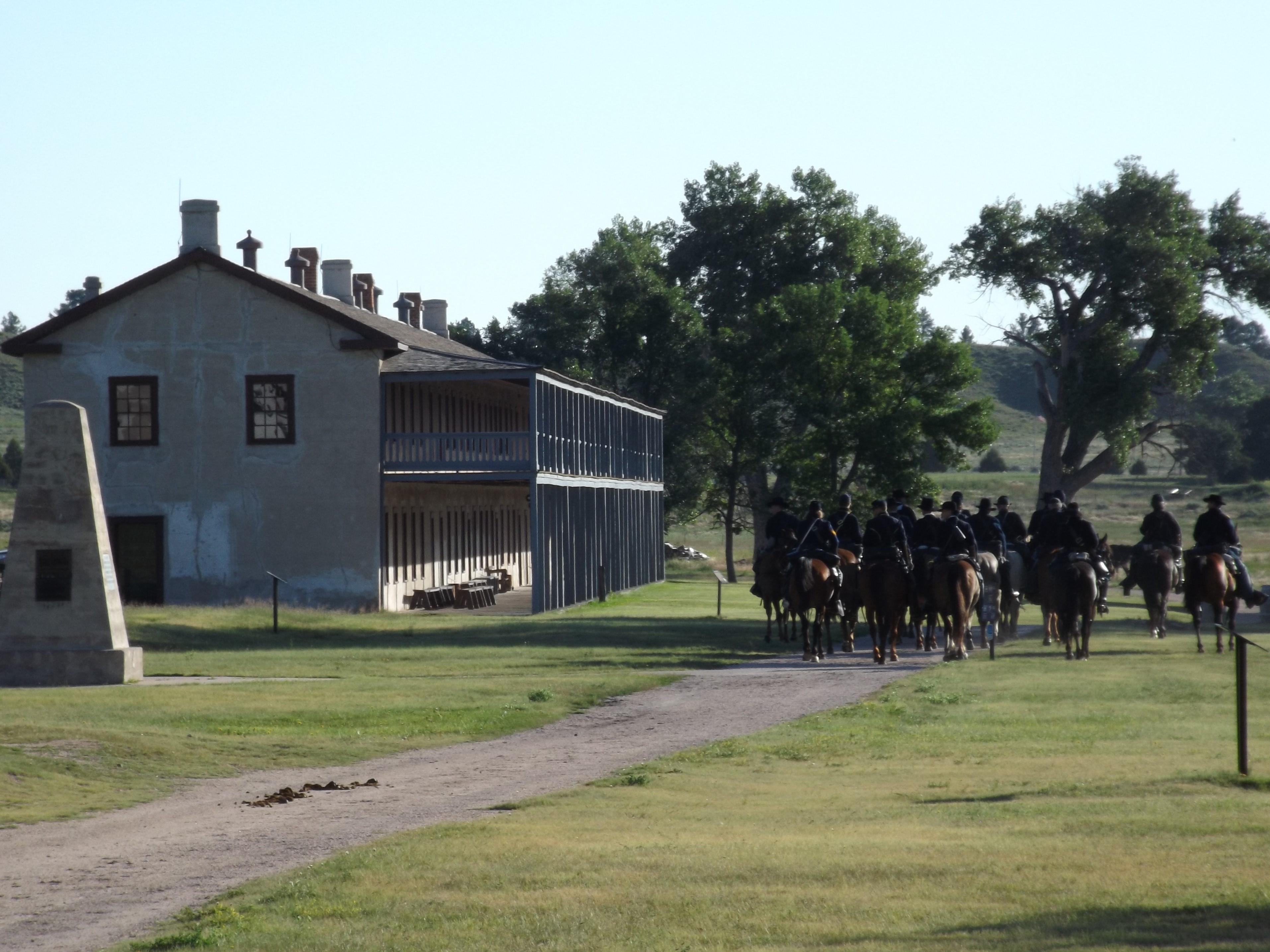 A group of mounted individuals ride hors near a concrete historic structure.