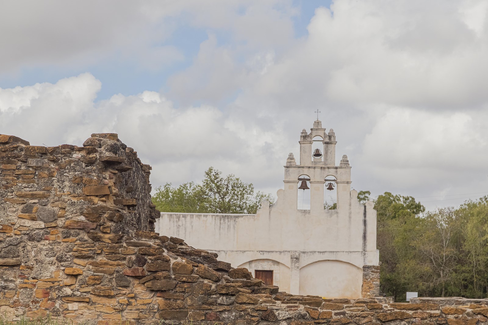 White frescoed church with a stone ruin to the left in the foreground.