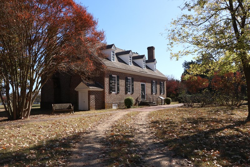A red brick building surrounded by trees and a dirt path leading to the building