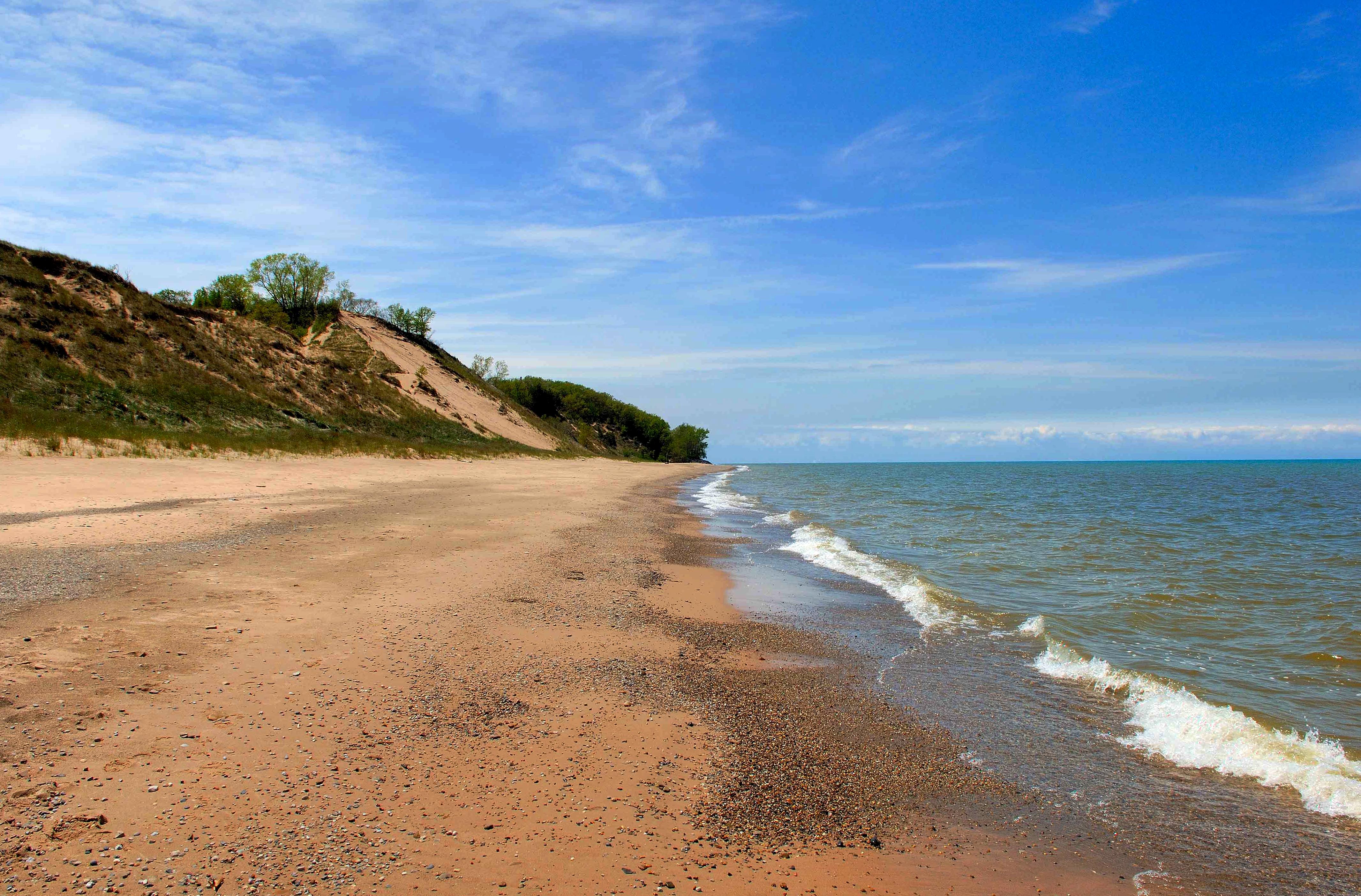 Michigan Lake beach with green grassy dunes in the background, under a blue sky.