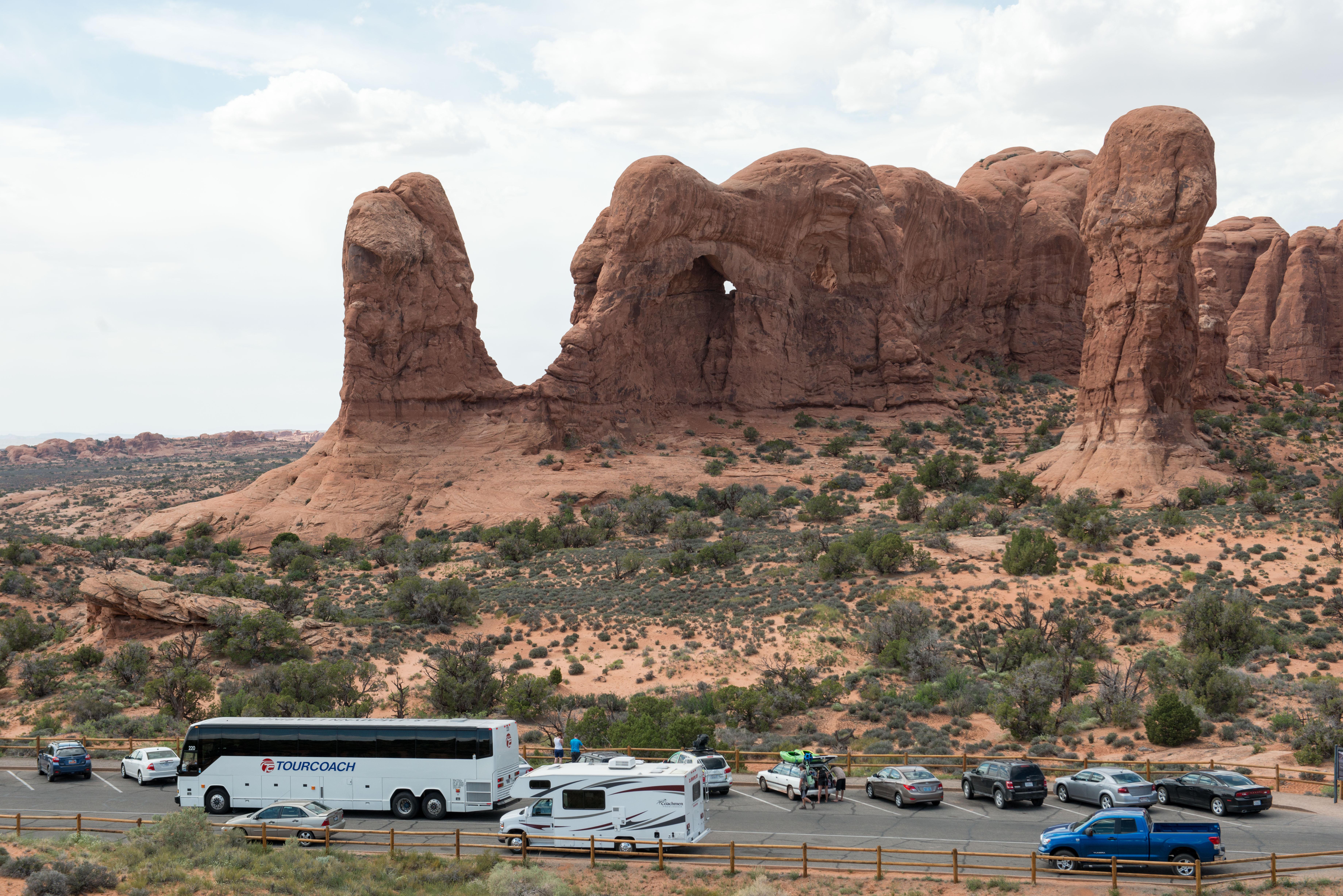 a bus, RV and several cars parked before tall rock formations
