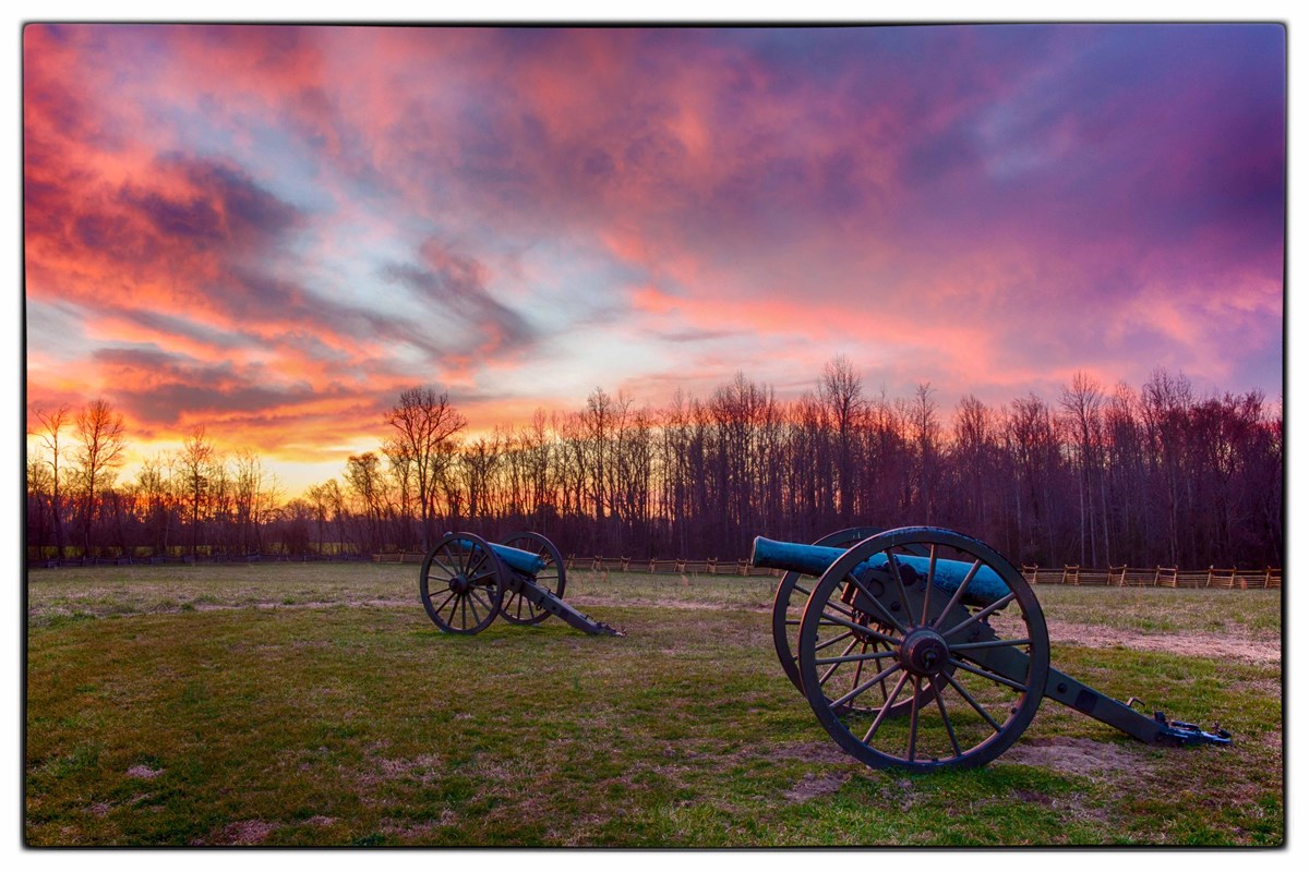 Two weathered bronze Civil War cannons in a grassy field, under a purple sunset sky.