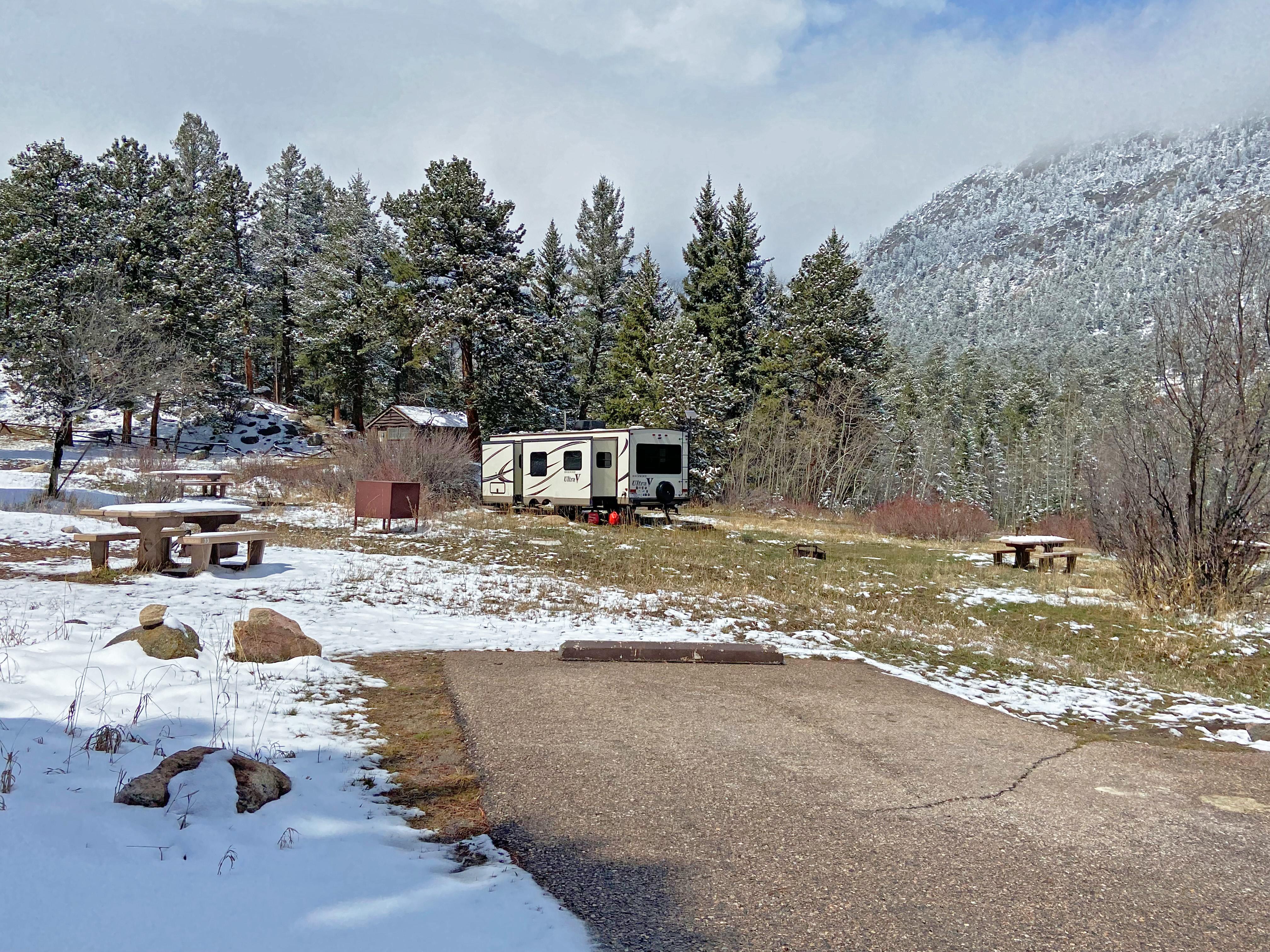 An RV is set up in a campsite and there is snow on the ground.