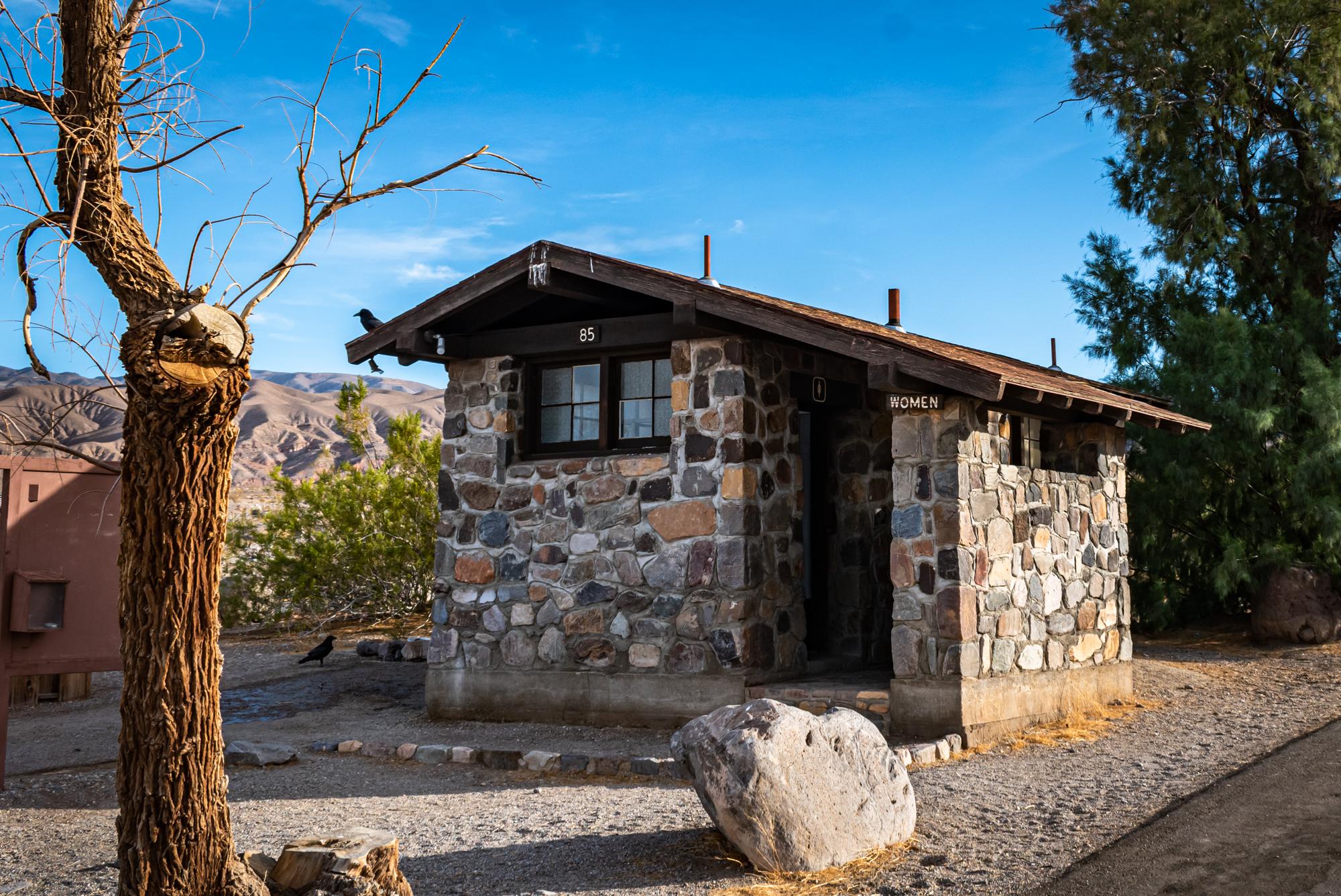 Stone building next to 4 ft wide rock path then asphalt. Space in front wall is entrance..